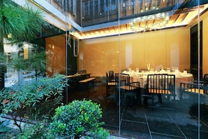 A modern dining area with glass walls, a chandelier, and indoor plants.