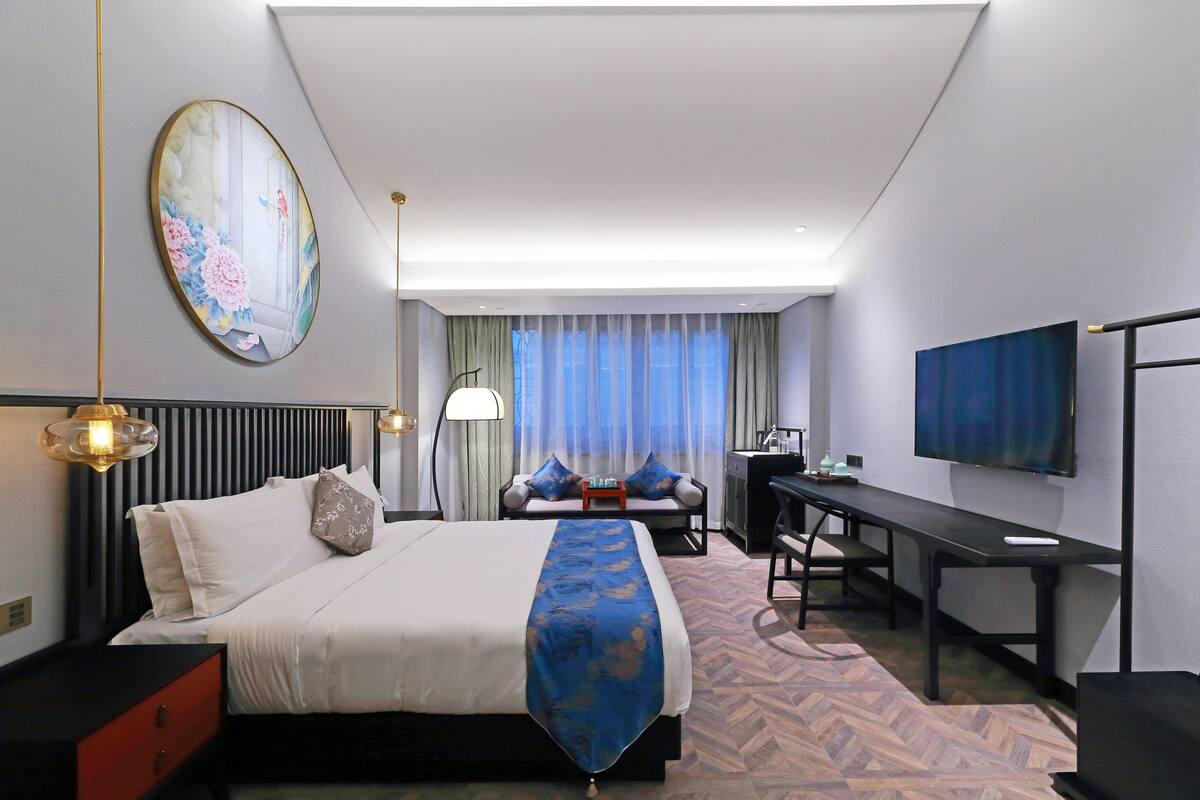 A hotel room with a bed, a desk, a TV, and a large window with curtains.