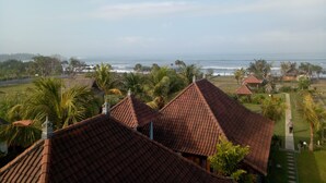 A coastal view with traditional tiled roofs, palm trees, and a clear sky. - Emir surfcamp (Pekutatan)