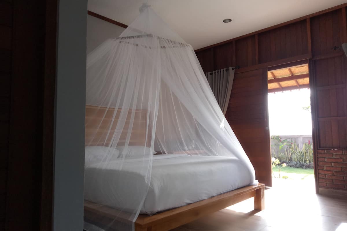 A bed with a white canopy in a room with wooden walls and a view of the outdoors.