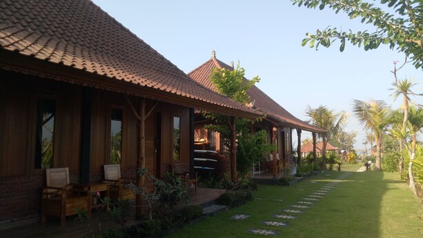 A traditional wooden building with a tiled roof, a covered outdoor seating area, and a well-maintained garden with a stone pathway. - Emir surfcamp (Pekutatan)