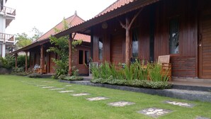 A row of wooden houses with tiled roofs, a well-maintained lawn, and stepping stones leading to the entrance. - Emir surfcamp (Pekutatan)