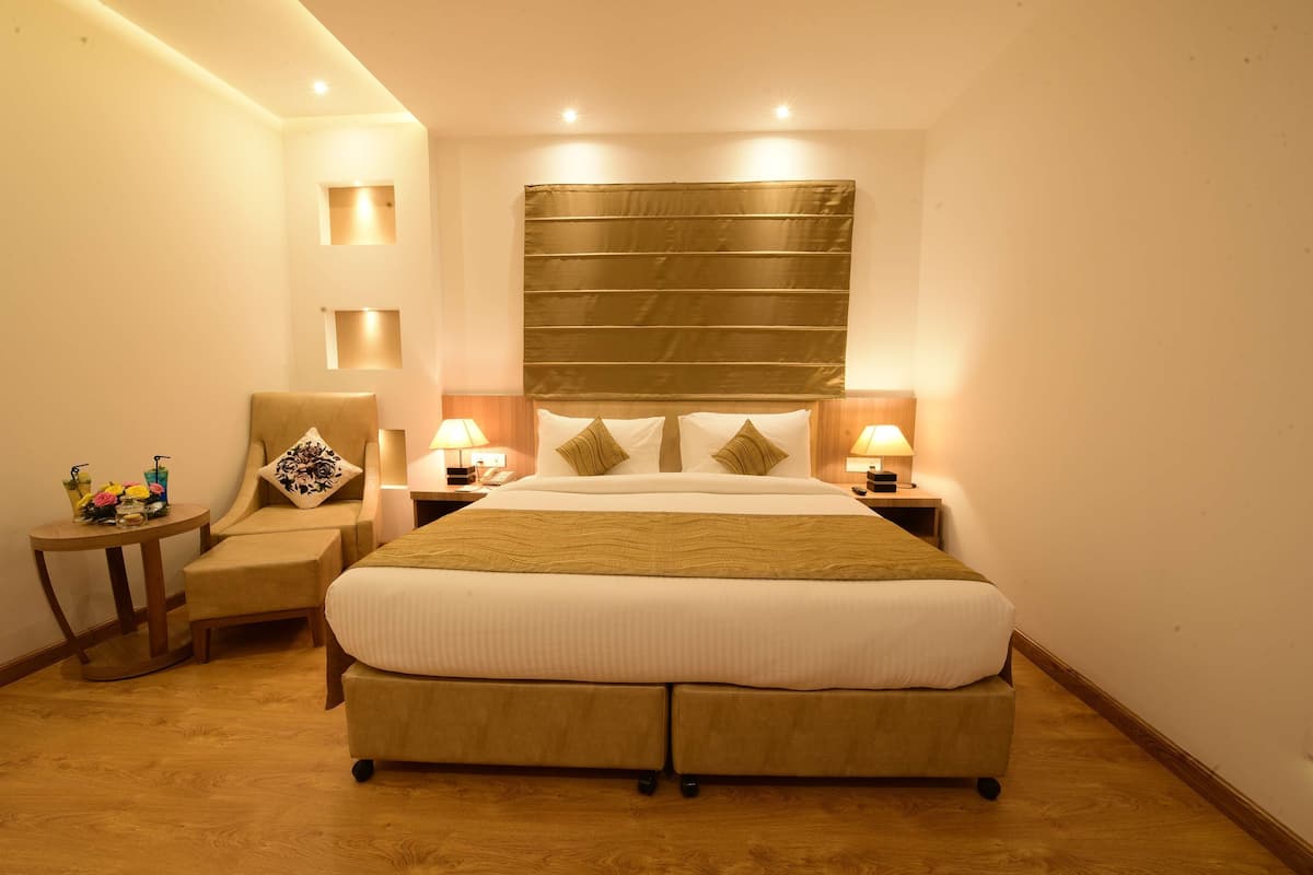 Een hotelkamer met een groot bed, twee nachtkastjes met lampen, een stoel en een tafeltje met een bloemenvaas.