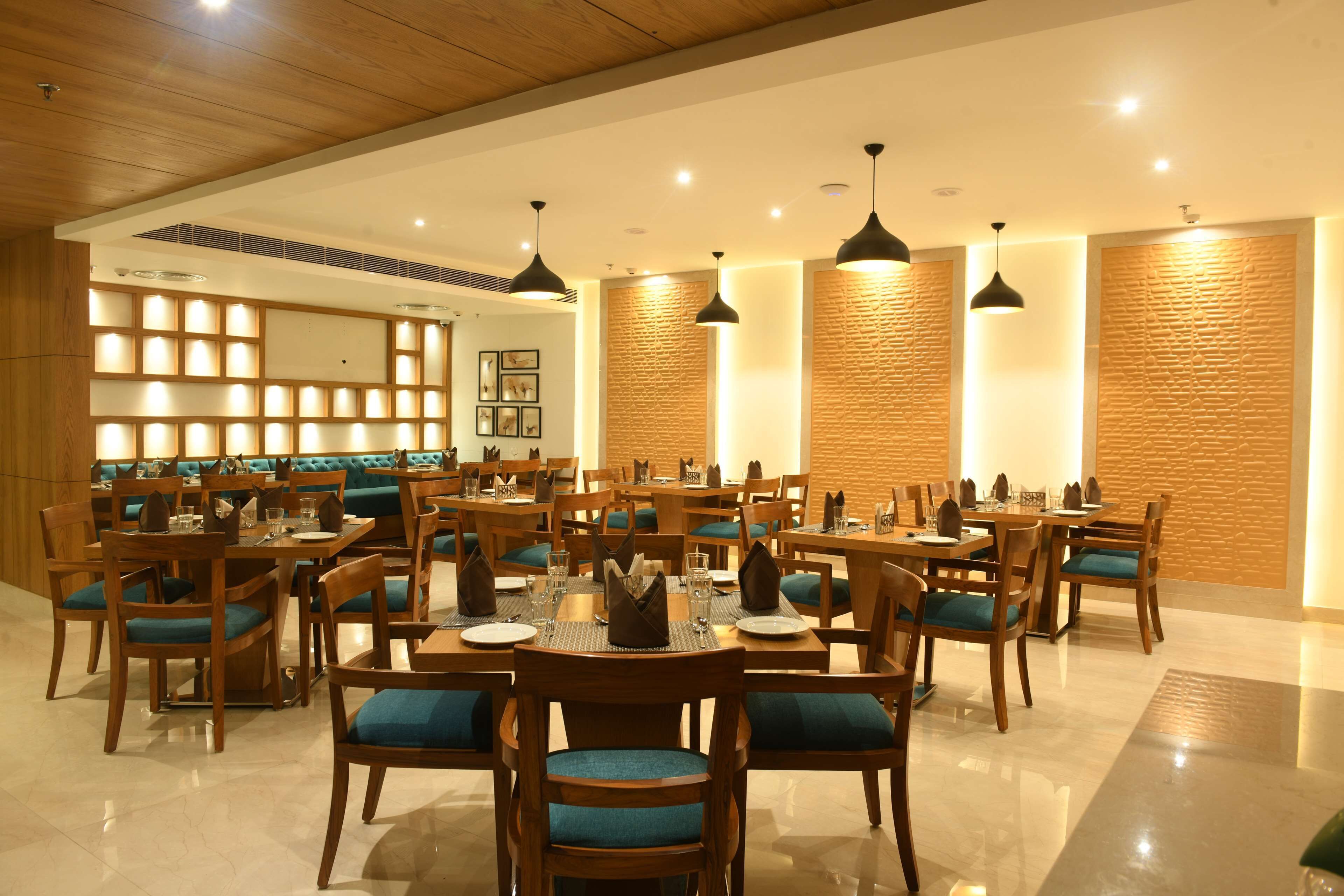 A spacious dining area with multiple tables and chairs, wooden paneling on the walls, and pendant lighting.