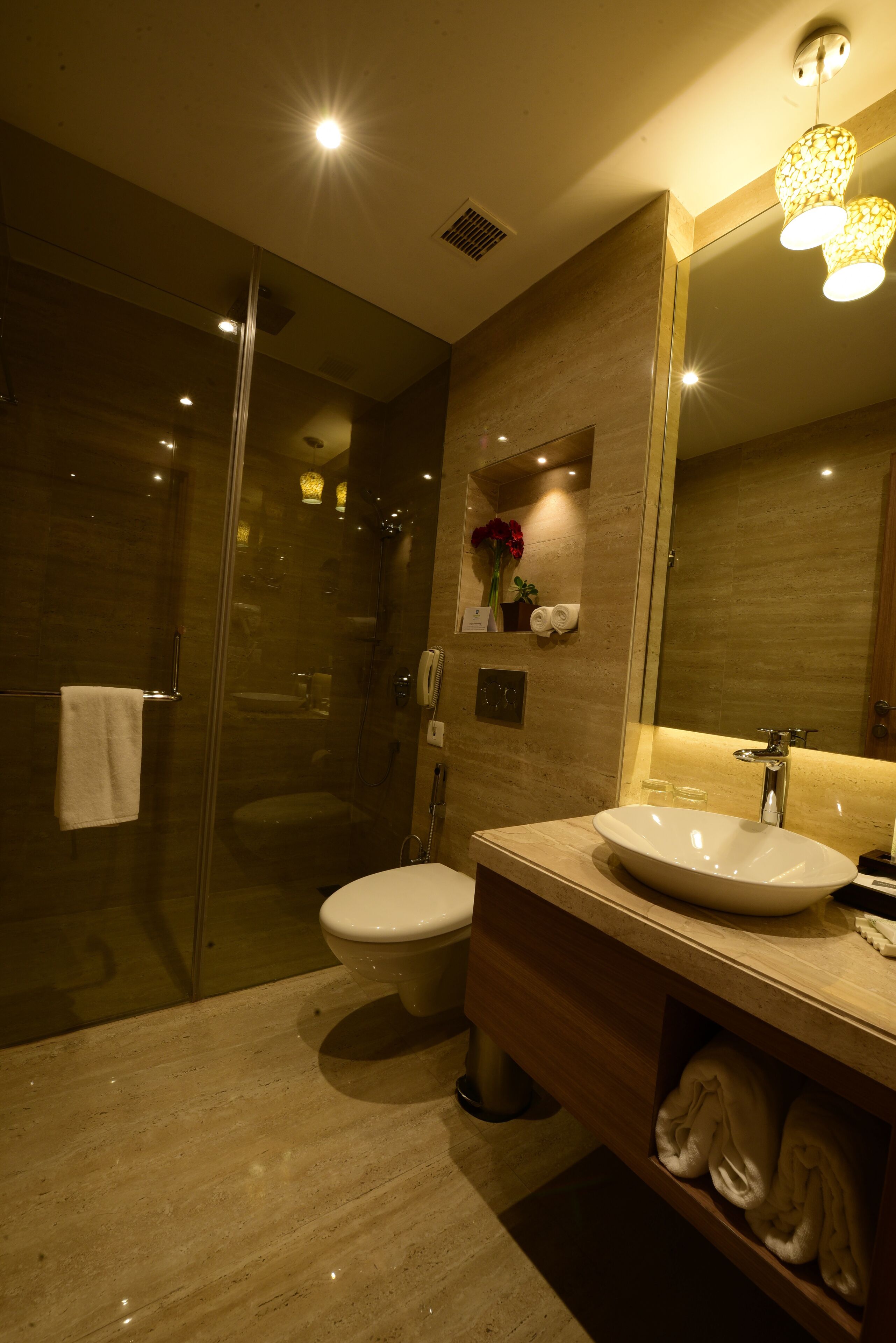 Un baño moderno con ducha envuelta en cristal, inodoro blanco y un espejo grande sobre el lavabo.