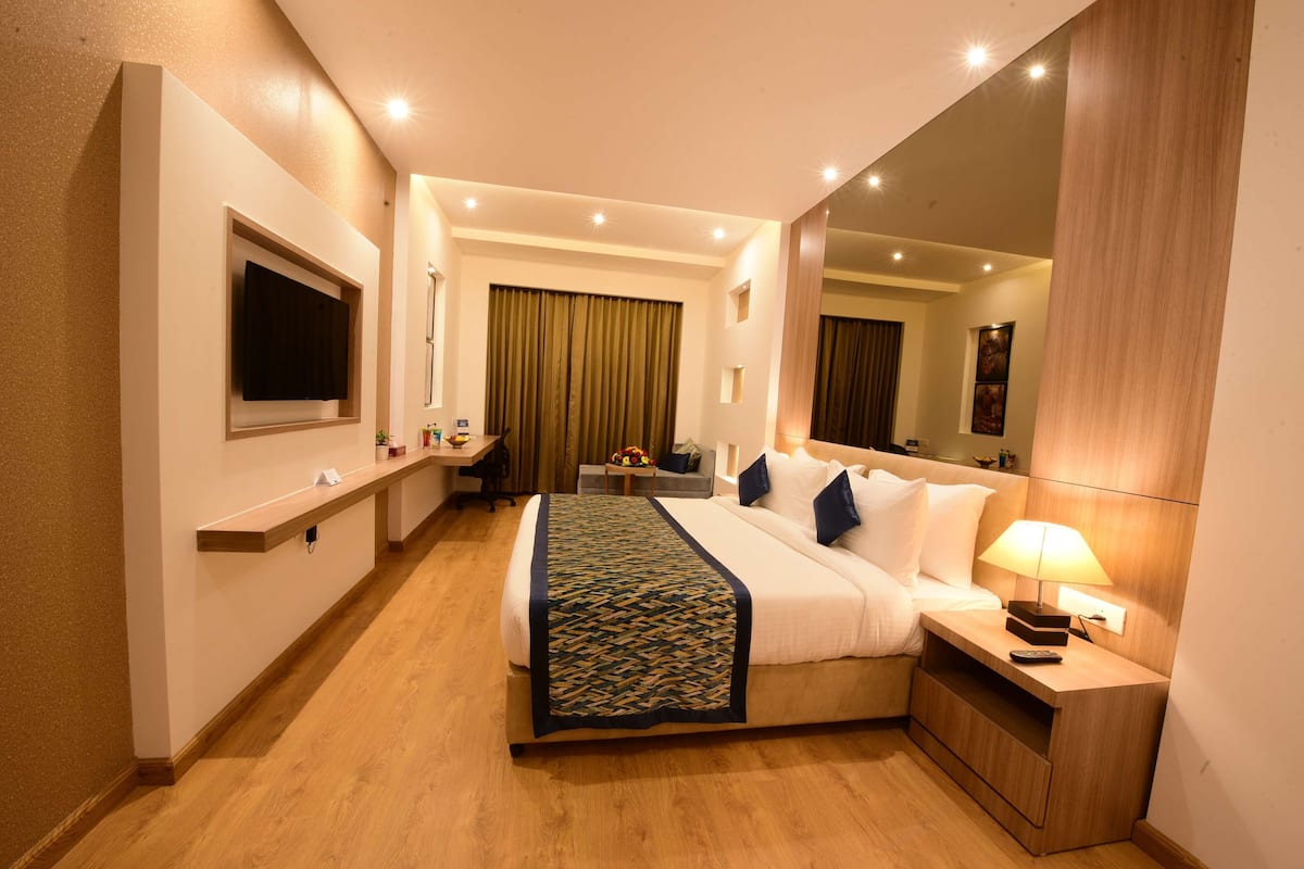 Een hotelkamer met een groot bed, nachtkastje, lamp en een spiegel.