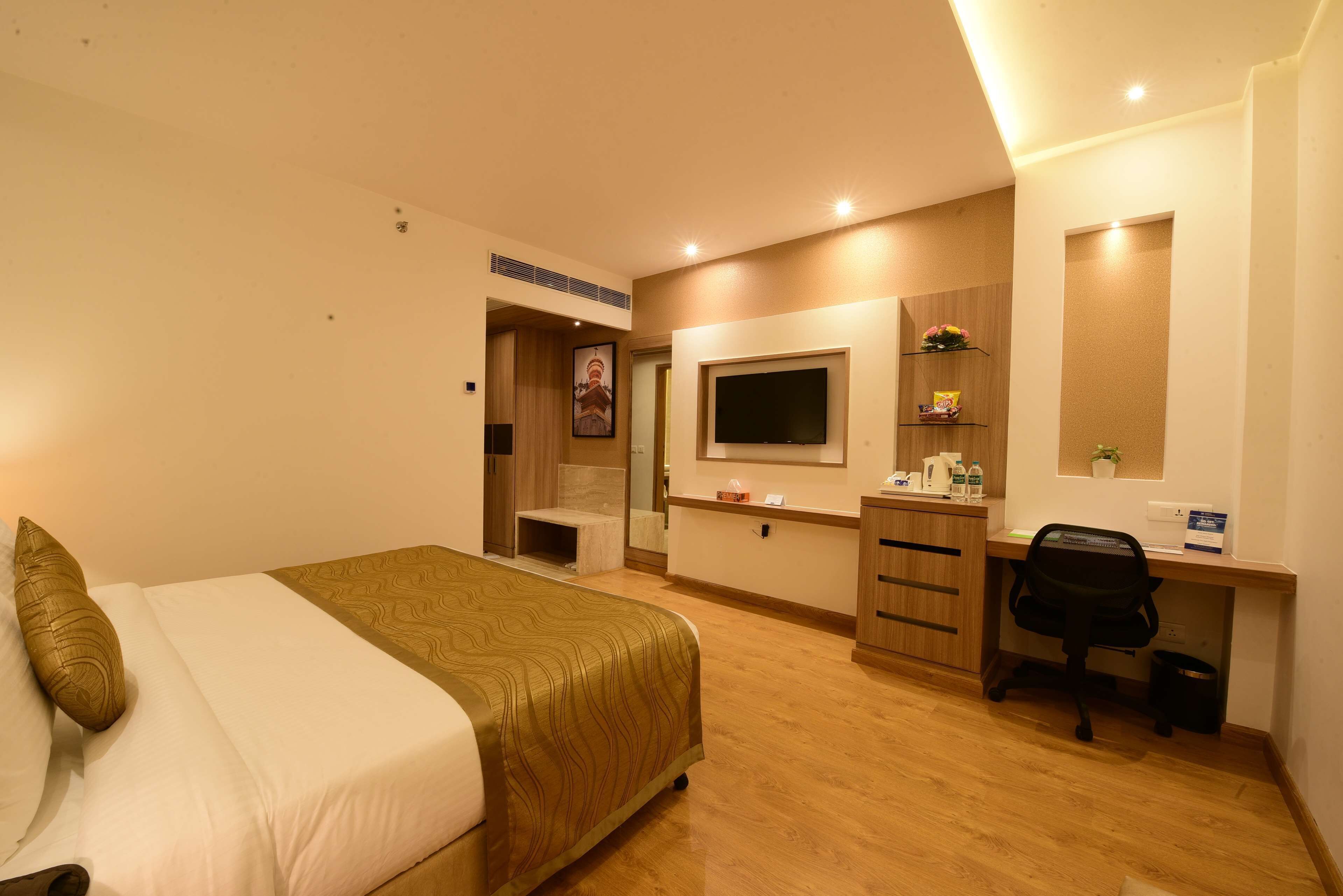 Habitación de hotel con cama, escritorio, silla, televisor y baño pequeño.
