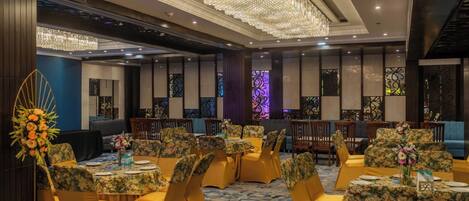 Un salón de banquetes con mesas redondas, sillas amarillas y una lámpara de araña grande.