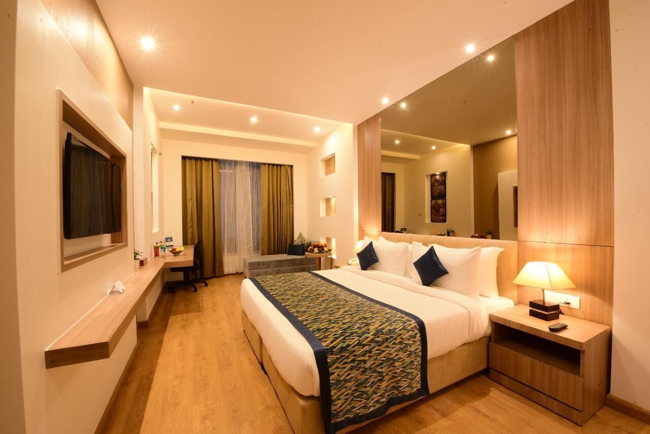 A hotel room with a large bed, bedside tables, a desk, and a mirror.
