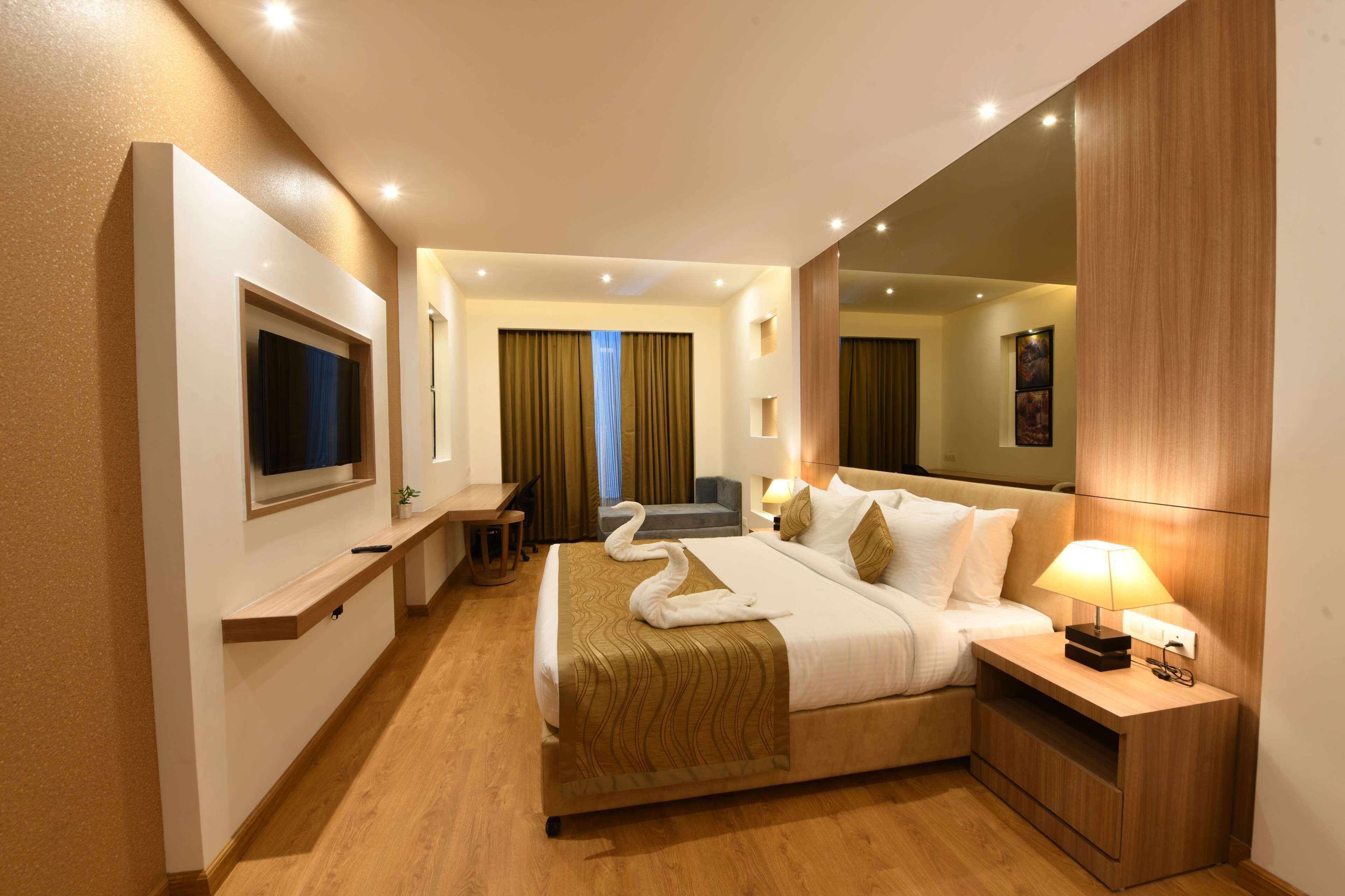 A hotel room with a large bed, a desk, a chair, a TV, and a mirror.