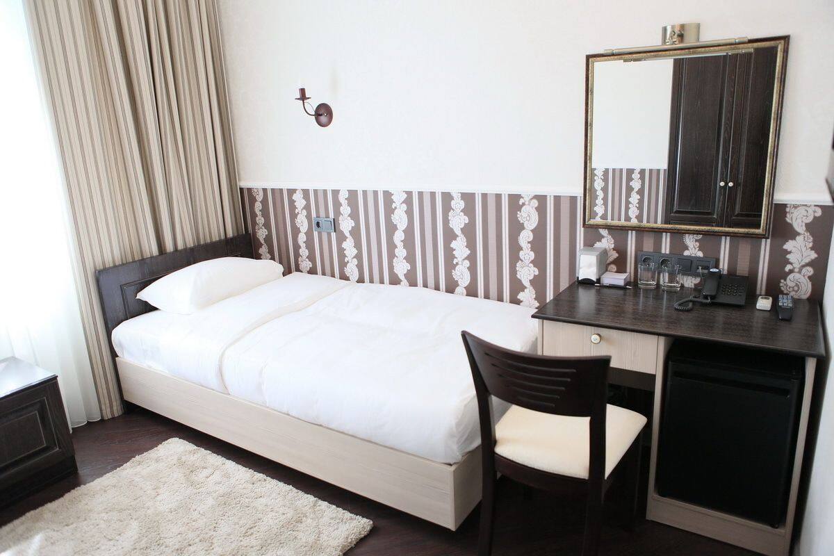 Une chambre d’hôtel comprenant un lit, un bureau avec une chaise, un miroir et une petite table avec une lampe.