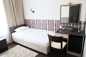 A hotel room with a bed, a desk with a chair, a mirror, and a small table with a lamp. - Mini Hotel D'Rami (Almaty)