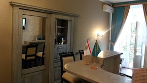A room with a dining table, chairs, a flag, and a window with curtains. - Mini Hotel D'Rami (Almaty)
