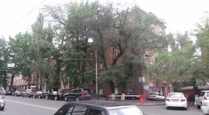 A street view with parked cars, trees, and a building with multiple windows and balconies. - Mini Hotel D'Rami (Almaty)