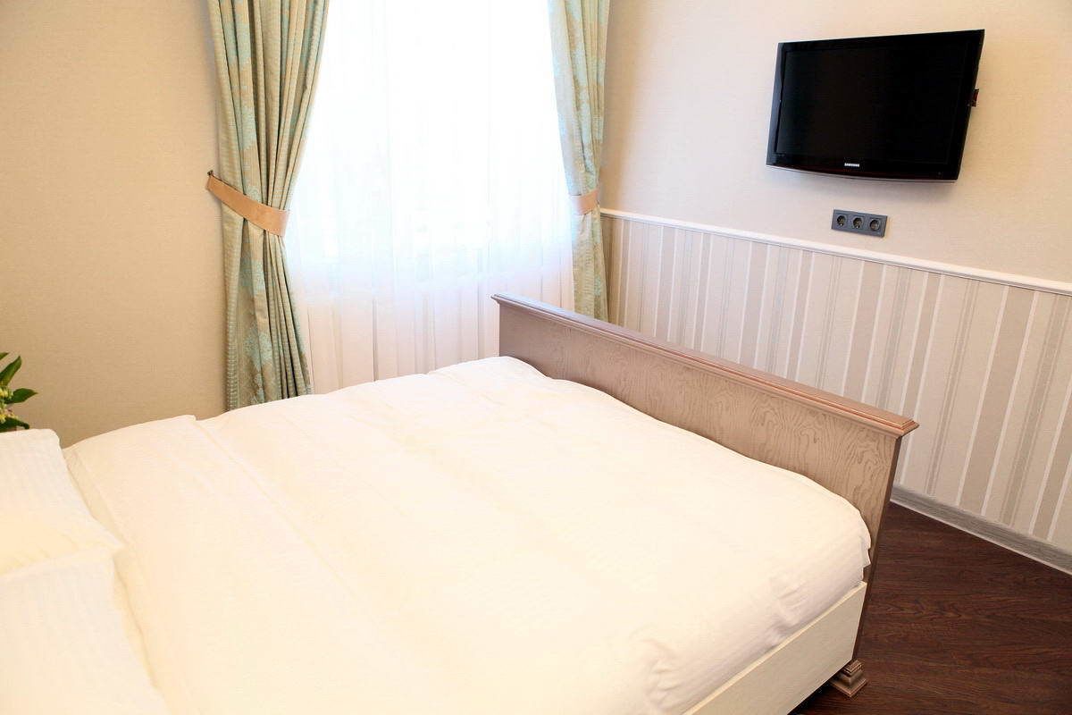 A bedroom with a bed, a television mounted on the wall, and a window with curtains.