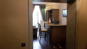 A narrow hallway leading to a kitchen area with a counter, chairs, and a television. - Mini Hotel D'Rami (Almaty)