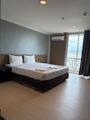 A hotel room with a bed, a nightstand, an air conditioning unit, and a view of the outside. - J & Y Lodge Hotel (Chonburi)