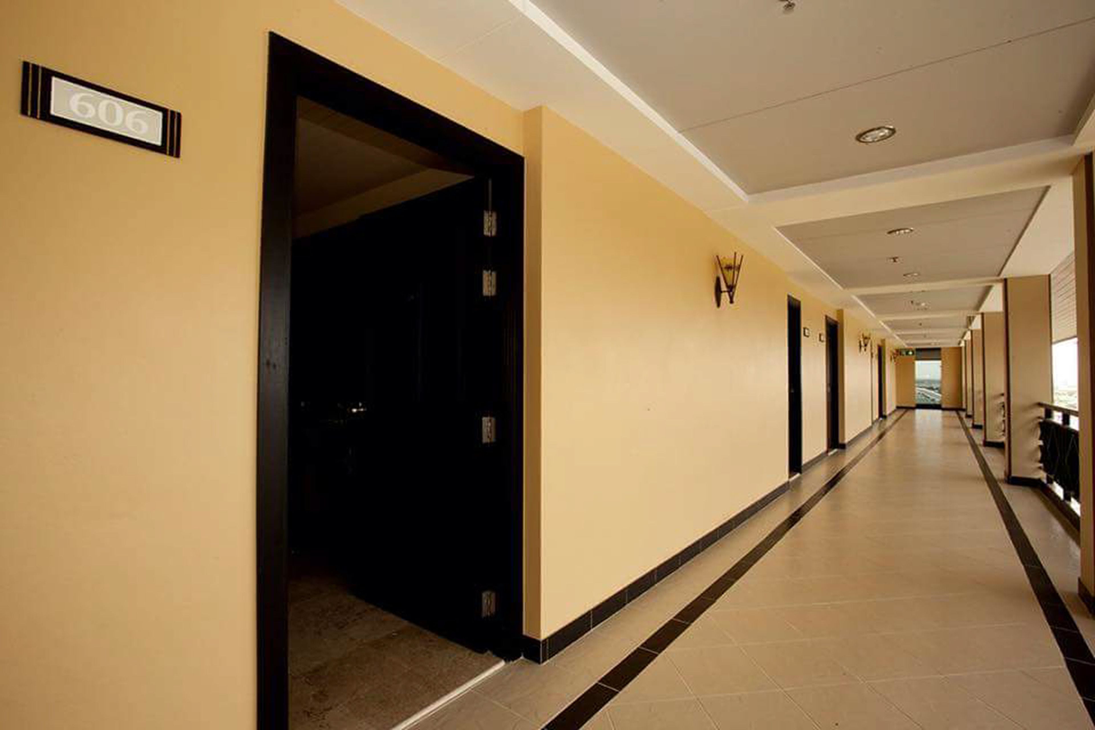 Un pasillo de hotel con un cartel que indica la habitación número 606. El pasillo tiene suelo de baldosas y paredes con una decoración en tonos claros.