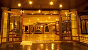 A spacious lobby with a wet floor sign, large glass doors, and a central fountain. - J & Y Lodge Hotel (Chonburi)