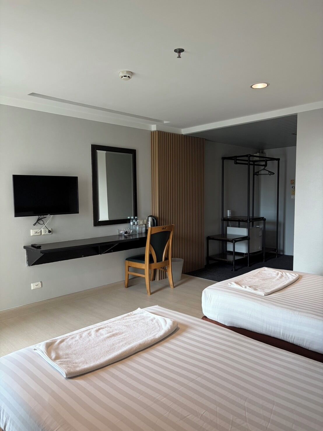 Habitación de hotel con dos camas, un escritorio con silla, televisión, espejo y armario.