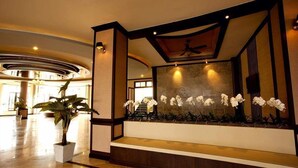 A lobby with a reception desk, a large potted plant, and a wall-mounted orchid display. - J & Y Lodge Hotel (Chonburi)