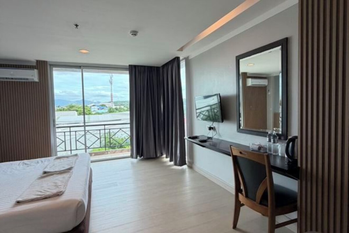 A hotel room with a bed, a desk, a chair, a TV, and a balcony with curtains.