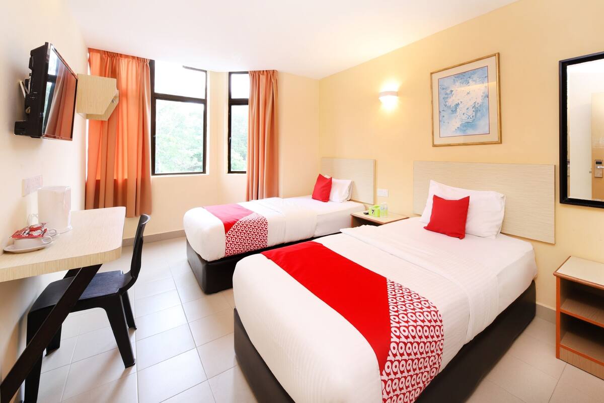 Une chambre d’hôtel avec deux lits, un bureau, une chaise, une télévision et une fenêtre avec des rideaux.