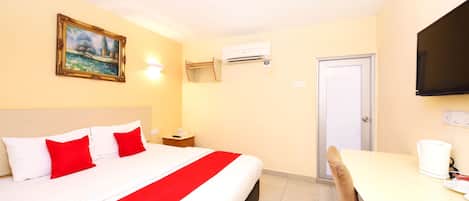 A hotel room with a bed, a desk, a chair, a painting, an air conditioner, and a television.