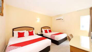 A hotel room with two beds, each with red and white bedding, a small table, and a wall-mounted air conditioner.