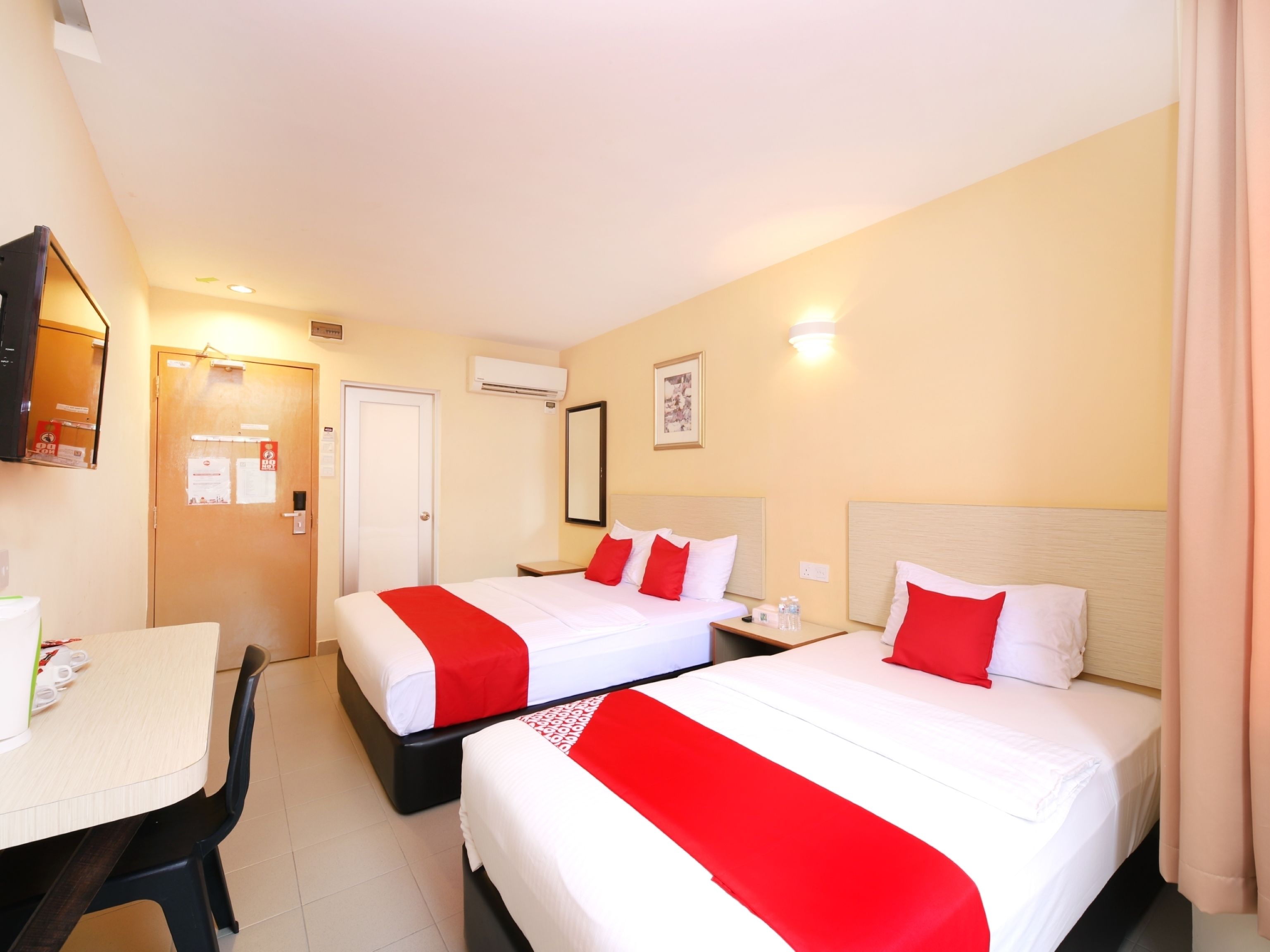 A hotel room with two beds, a desk, a chair, and a television.