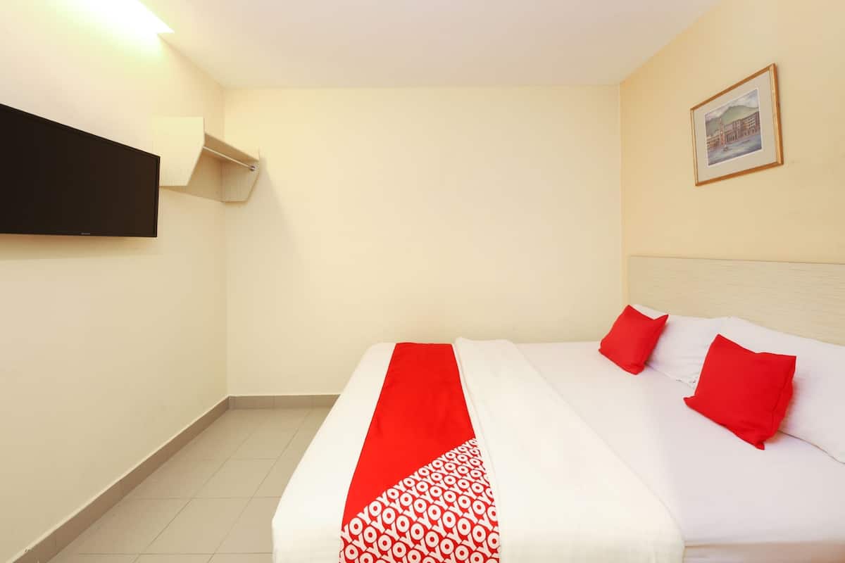 Une chambre d’hôtel avec un lit, un téléviseur à écran plat fixé au mur et un tableau encadré accroché au mur.