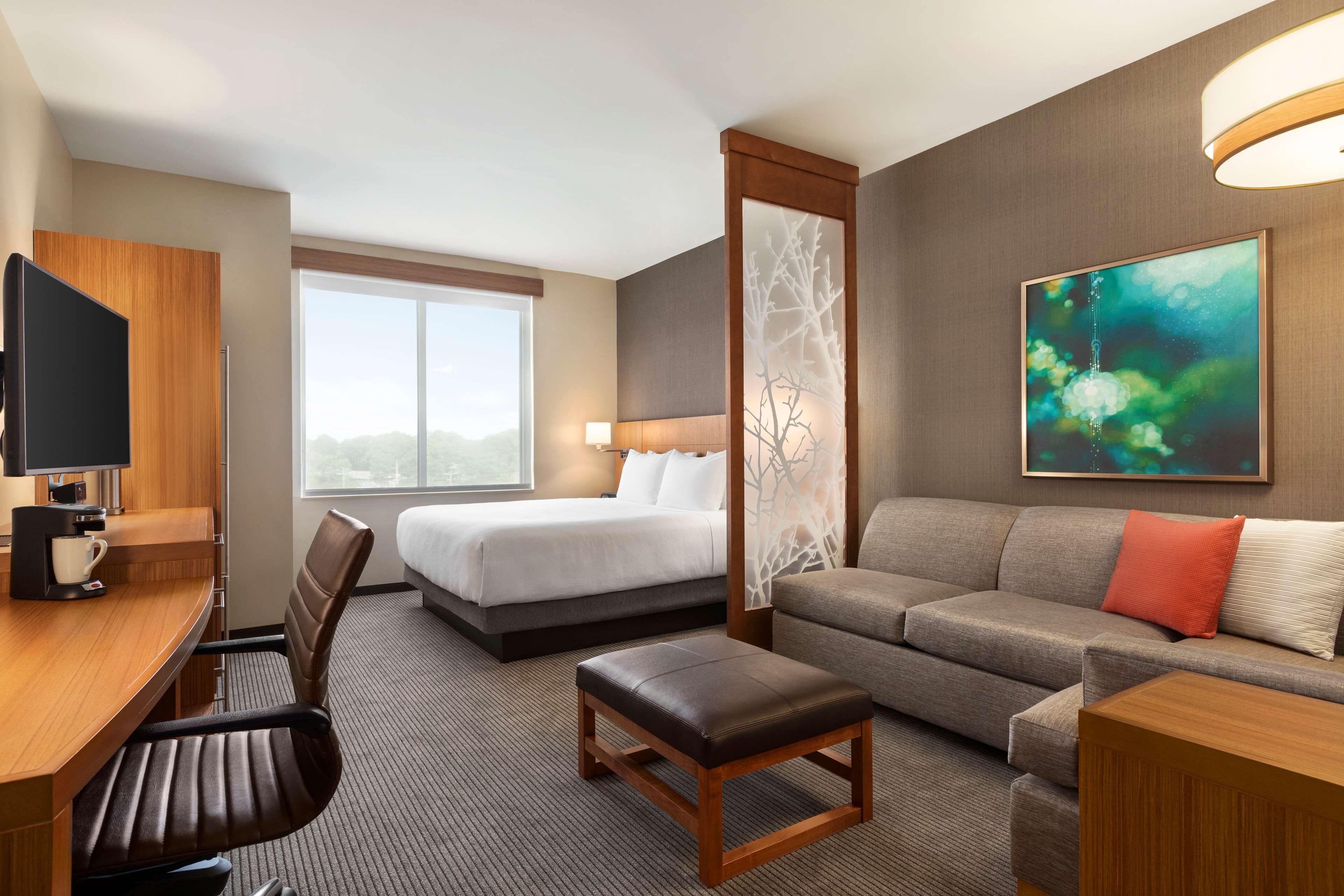 Quarto de hotel com cama, sofá, escrivaninha com cadeira, televisão e janela com vista.
