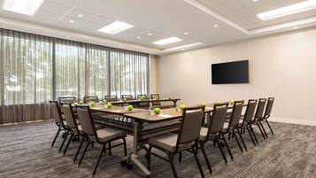 A conference room with a large table, chairs, a flat-screen TV, and a large window with curtains.