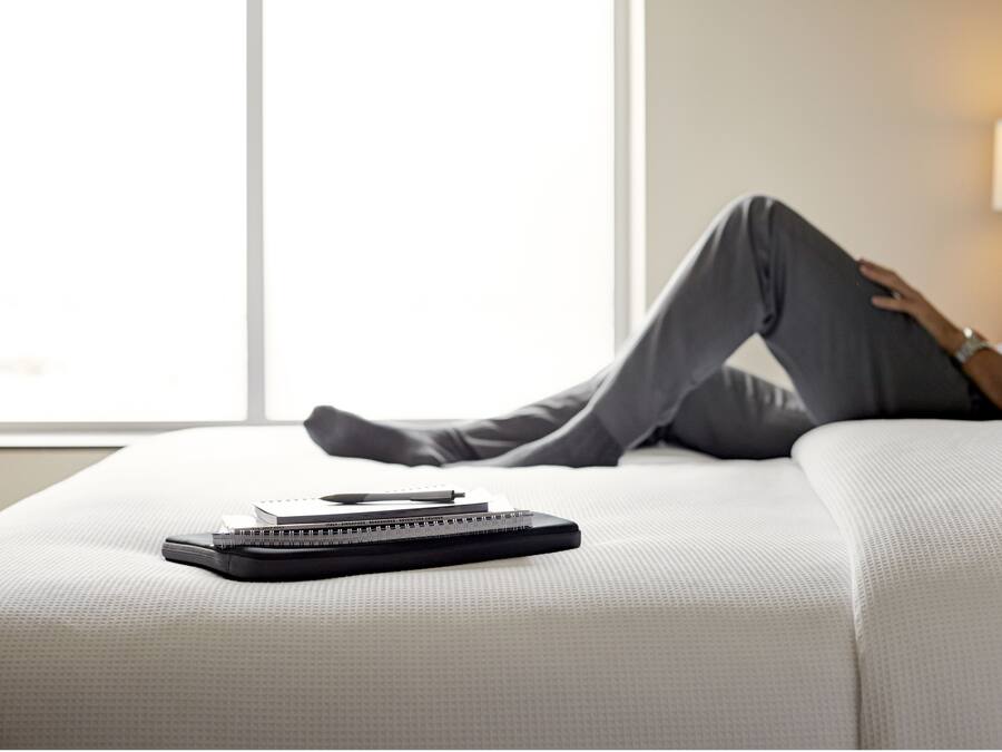 A person reclining on a bed with a notebook and pen on it.