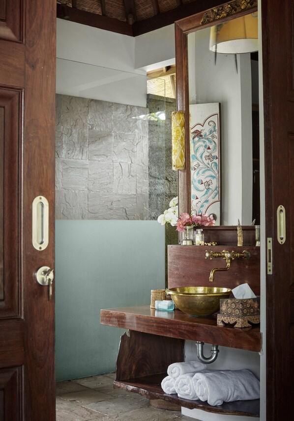 A bathroom with a wooden vanity, a brass sink, and a mirror.