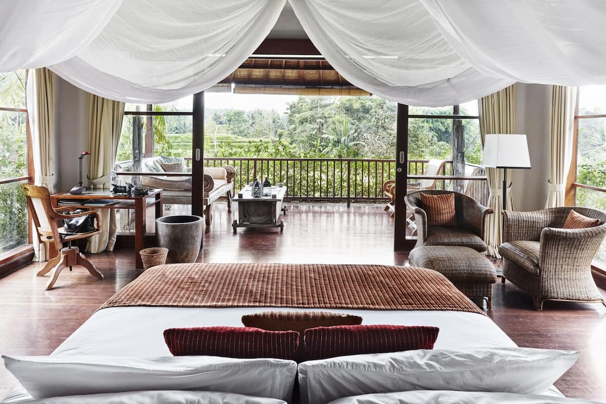 A spacious bedroom with a large bed, a desk, and a balcony with wicker furniture.