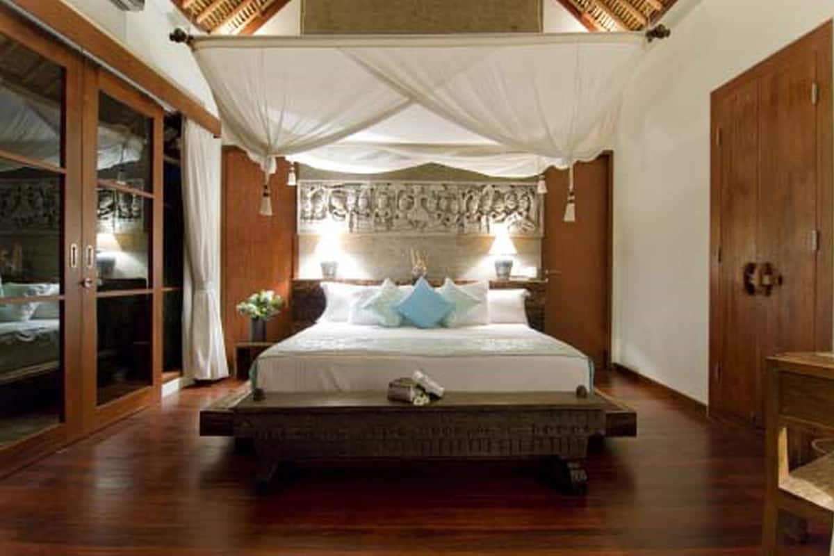 A bedroom with a large bed, wooden flooring, a canopy, and a decorative headboard.