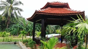 A traditional pavilion with a tiled roof, surrounded by lush greenery and a small pond. - Areca Garden Bungalow (Phu Quoc)