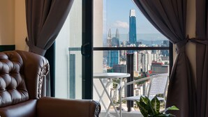 A room with a leather chair, a small table, and a potted plant. A balcony with a view of a cityscape is visible through the window. - J DUPION Boutique Suites by NowHere (Kuala Lumpur)