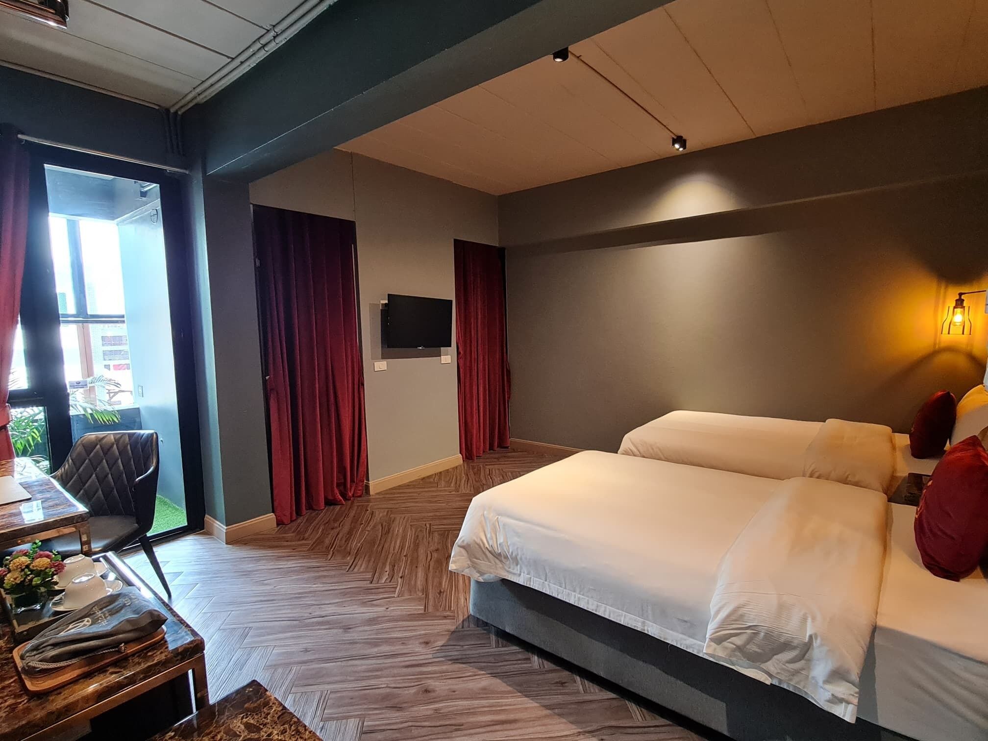 A hotel room with a large bed, a desk with a chair, a TV mounted on the wall, and a window with curtains.