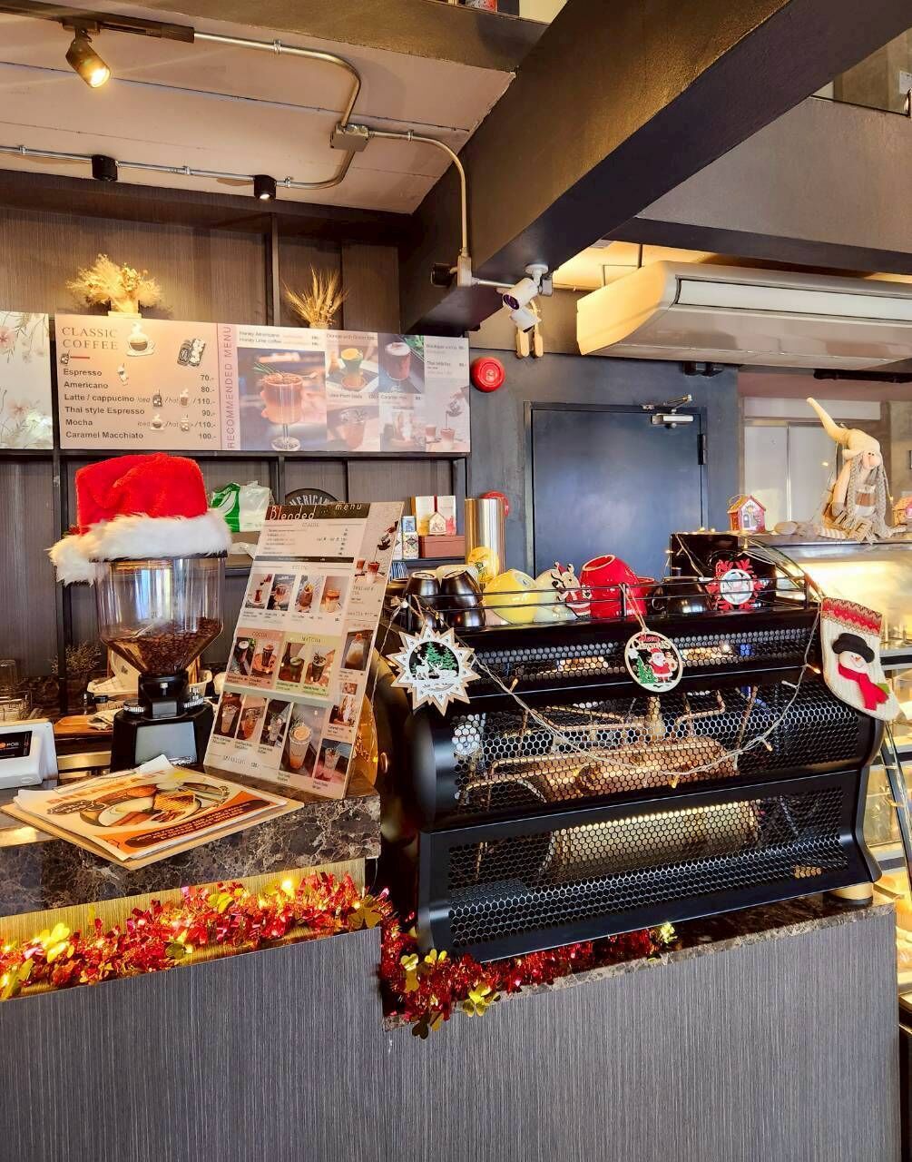 Ein Tresen eines Cafés mit einer Kaffeemaschine, Speisekarten und festlicher Dekoration.