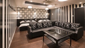 A modern room with a sofa, a glass coffee table, a bed with patterned pillows, and a striped wall. - Hotel Xenia Amagasaki - Adult Only (Amagasaki)