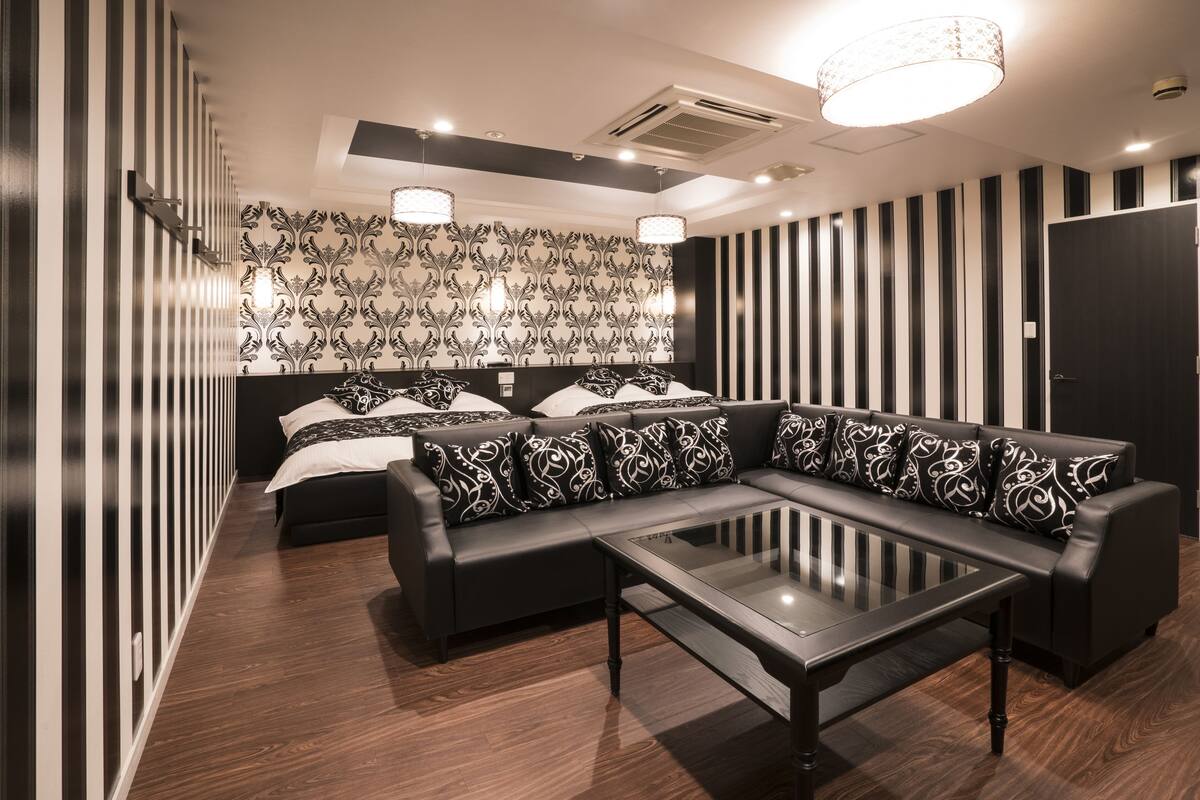 Una habitación moderna con un sofá, una mesa de centro de vidrio, una cama con almohadas estampadas y una pared a rayas.