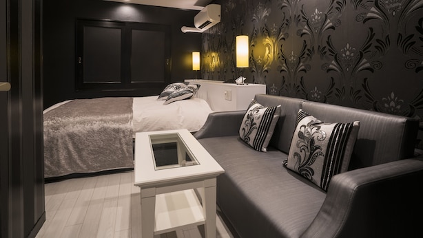A modern bedroom with a bed, a sofa, a bedside table, and a wall-mounted air conditioner. - Hotel Xenia Amagasaki - Adult Only (Amagasaki)