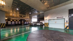 Un estacionamiento con suelo verde, un elevador para vehículos y un coche blanco estacionado cerca del elevador.