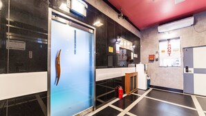 Un moderno vestíbulo de hotel con puerta de vidrio, mostrador de recepción y extintor en el suelo.