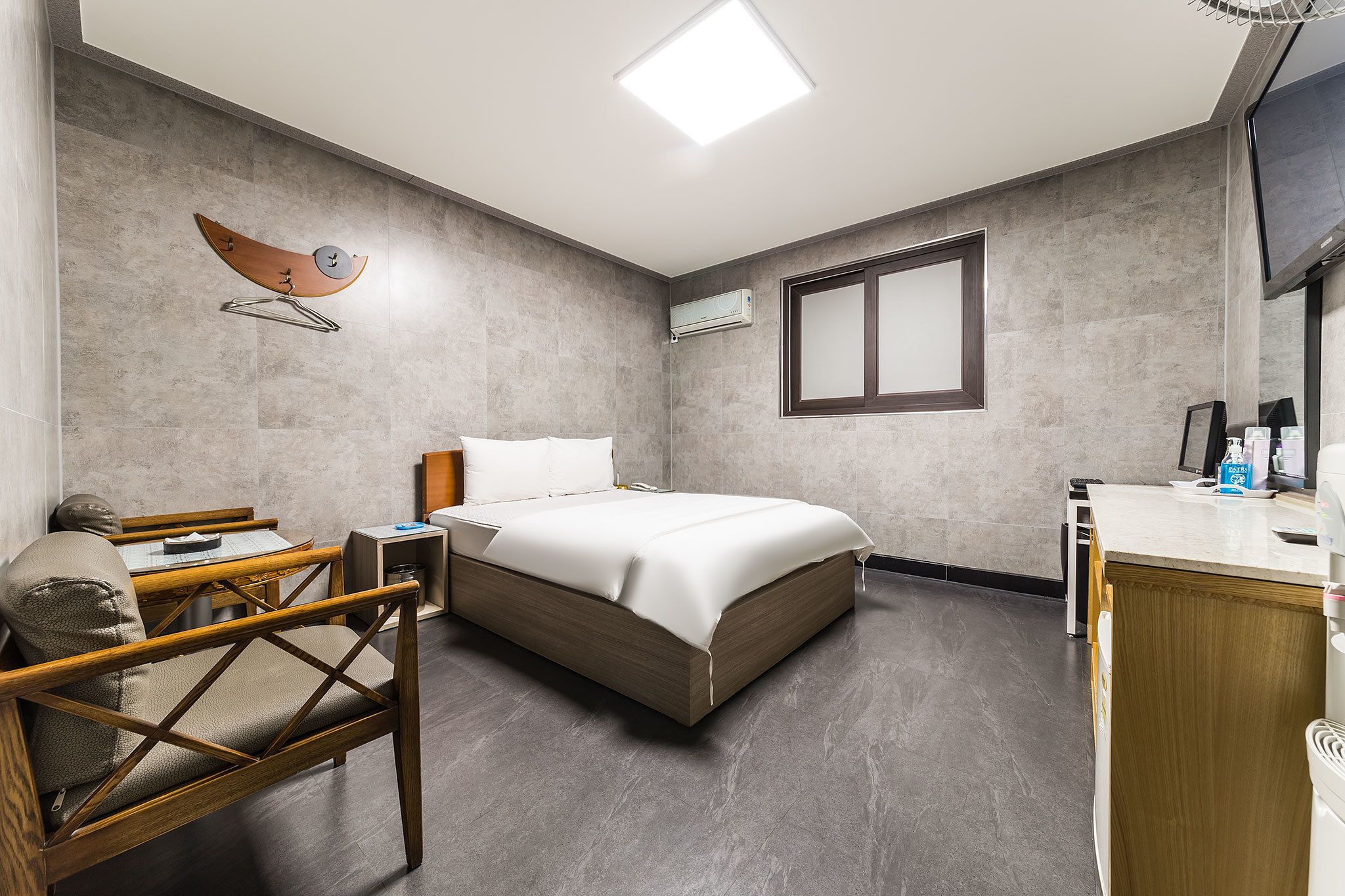 A modern hotel room with a bed, a desk, a chair, a TV, and an air conditioning unit.