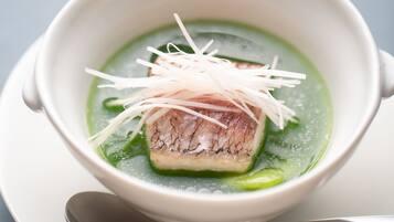 A bowl of soup with a piece of fish and shredded vegetables.