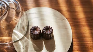 A wooden table with a glass and two small, dark-colored desserts.