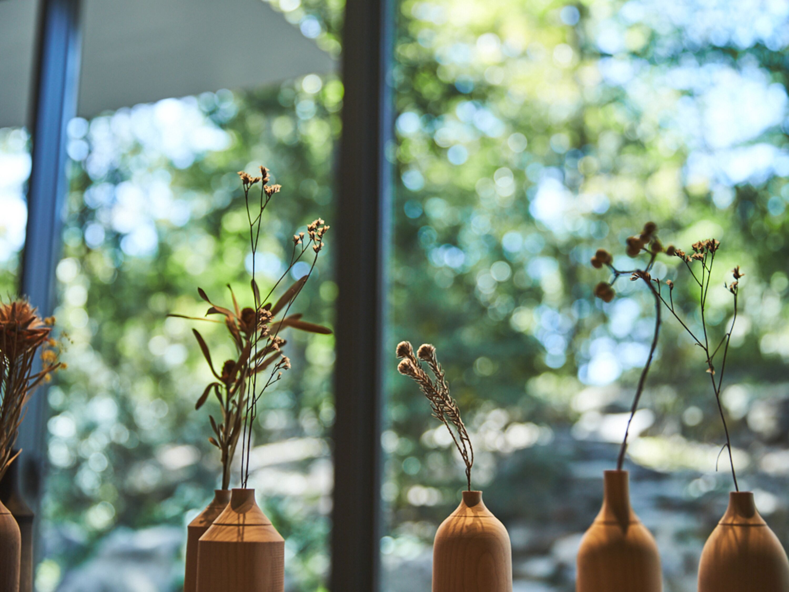 Four wooden vases with dried plants on a windowsill.